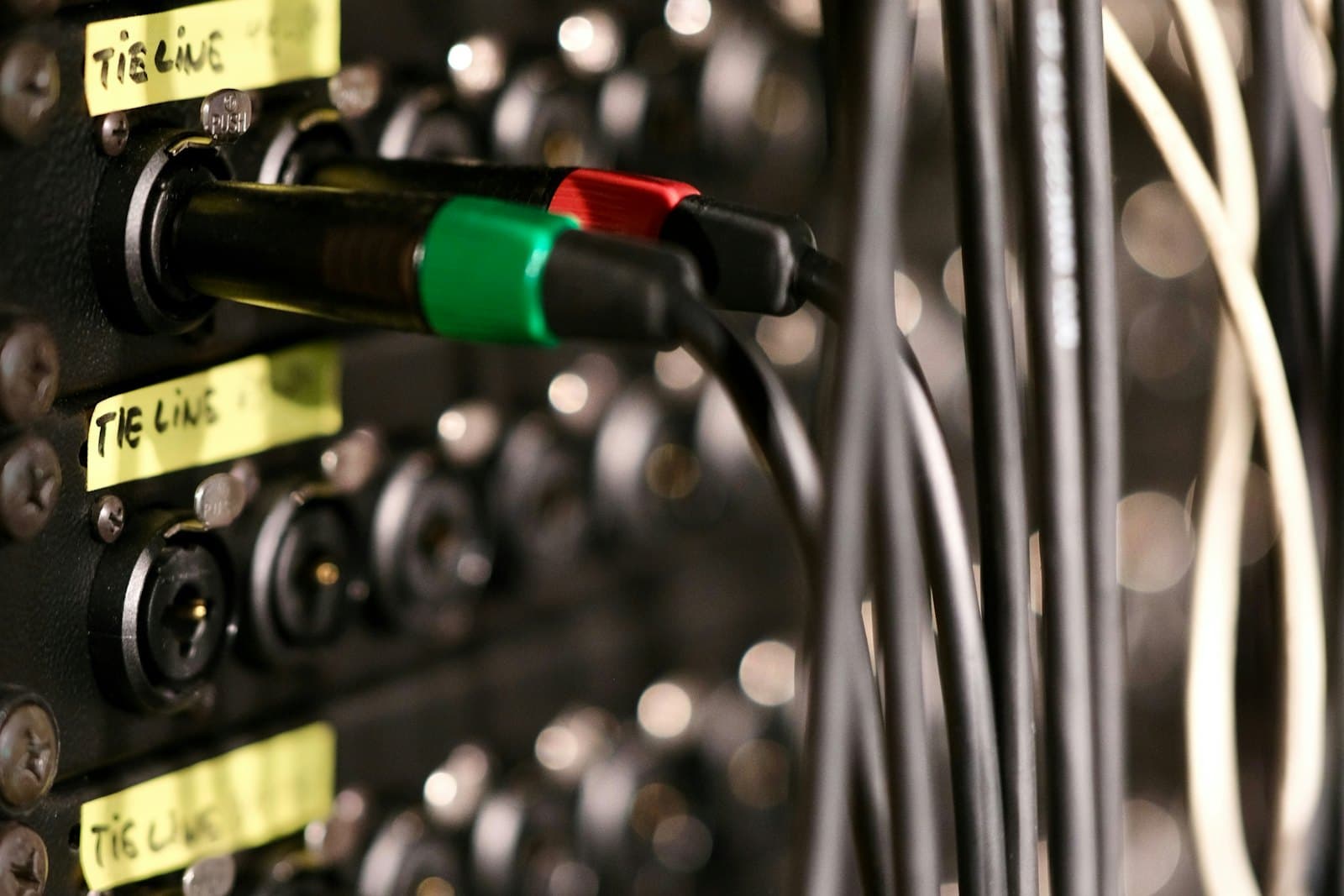 Close-up of an audio patch bay with hand-written “tie line” labels and colour-coded cables plugged into its jacks.